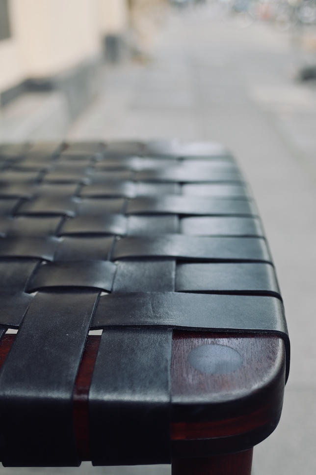 Detailansicht eines mit schwarzen Lederriemen im Leinwandmuster bespannten Designerstuhls